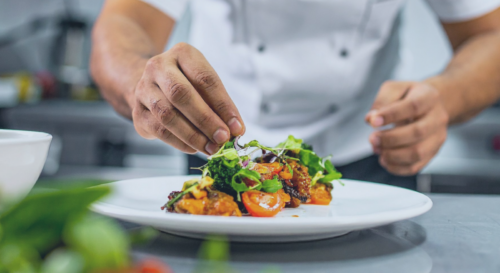 Koch richtet Essen auf einem Teller an visualisierend für 7 % Umsatzsteuer Speisen Gastronomie