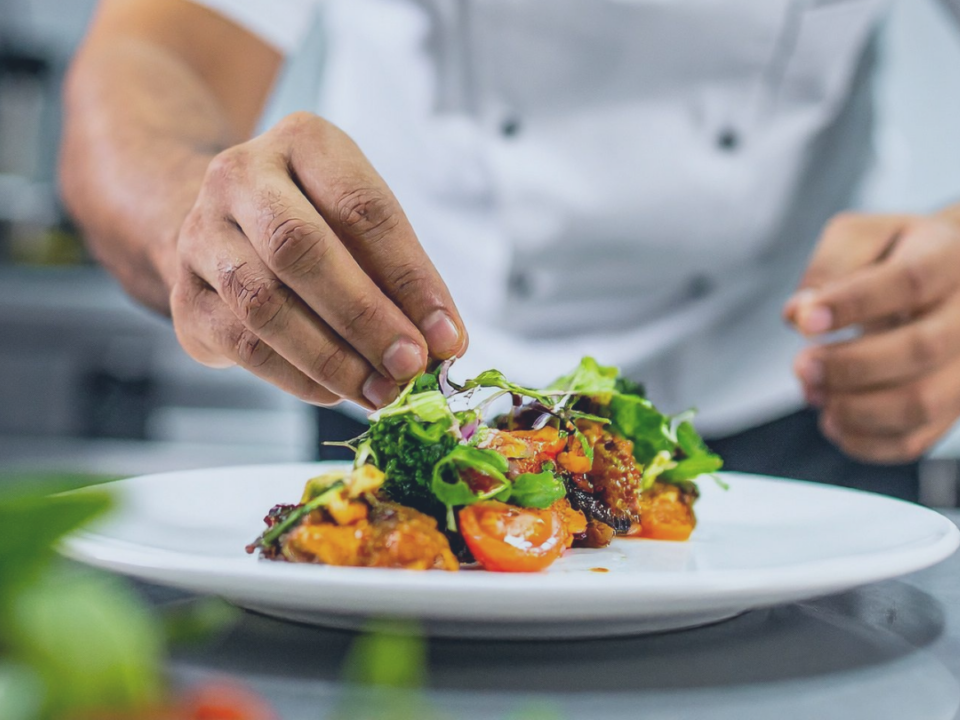 Koch richtet Speisen auf einem Teller an visualisierend für 7 % Umsatzsteuer Gastronomie