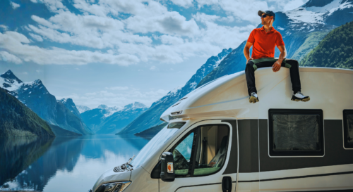 Mann auf Wohnwagen sitzend, Hintergrund Berge visualisierend für Privates Wohnmobil verkauft: Gewinn ist nicht zu versteuern