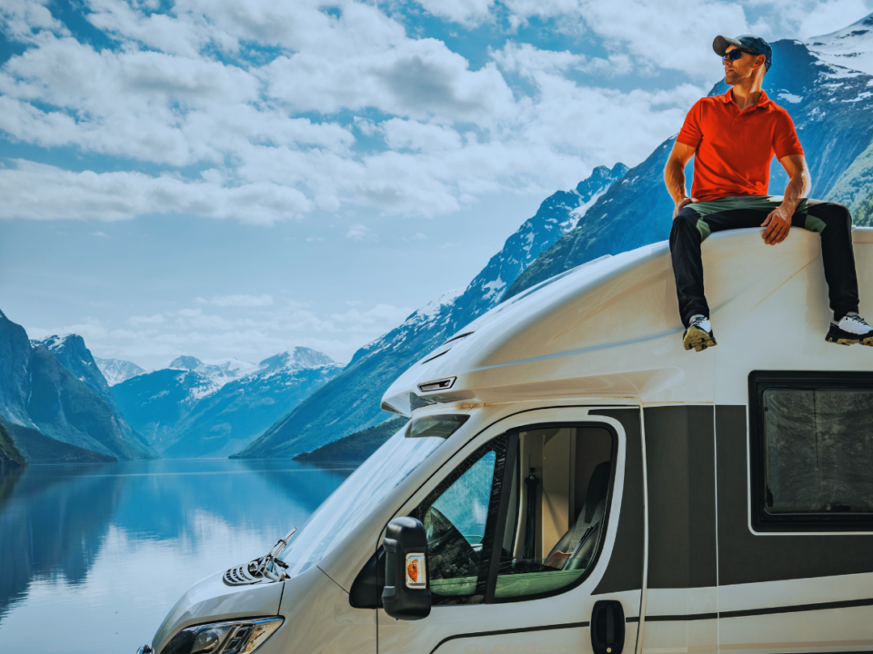 Mann auf Wohnwagen sitzend, Hintergrund Berge visualisierend für Privates Wohnmobil verkauft: Gewinn ist nicht zu versteuern