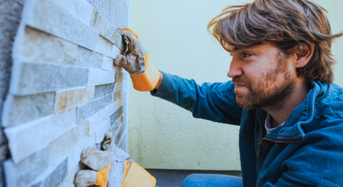 Handwerker, der eine Wand mit Steinen verkleidet visualisierende für Einnahmen auch bei Zahlung des Mieters an einen Dritten