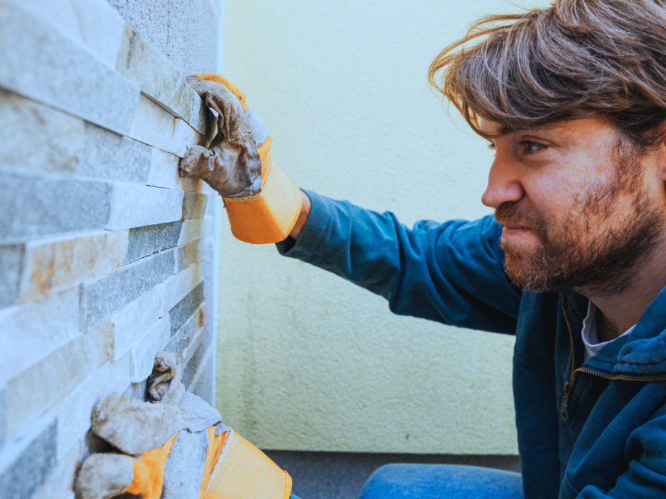 Handwerker, der eine Wand mit Steinen verkleidet visualisierend für Einnahmen auch bei Zahlung des Mieters an einen Dritten